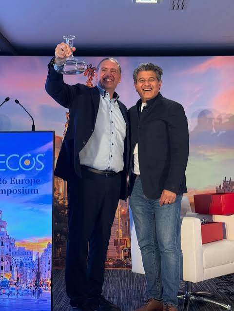 Michael Mrochen smiling on stage and raising a glass award beside another participant